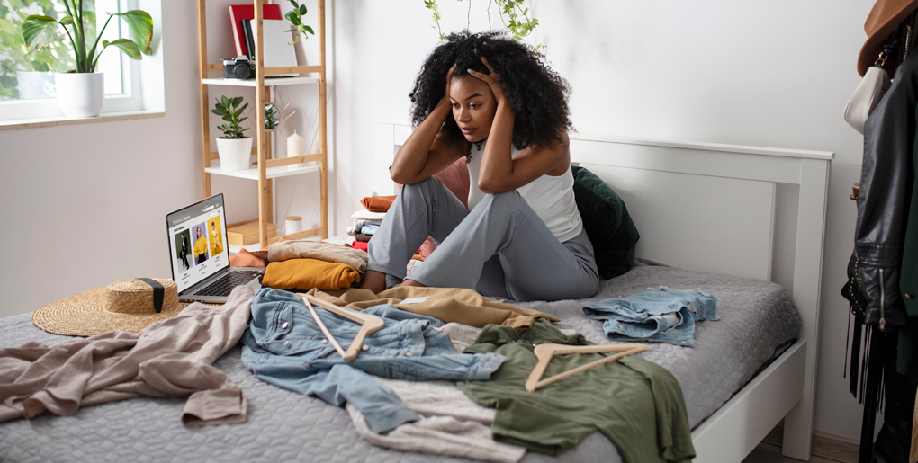 A woman looking overwhelmed in a cluttered bedroom, illustrating the psychological impact of disorganized living spaces on anxiety and sleep quality.