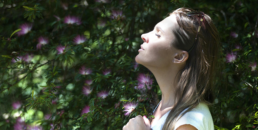 Woman breathing deeply in a garden, representing the fresh air and improved well-being that house cleaning services provide